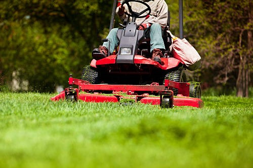 gardener in the park on a lawn cutting tractor machine